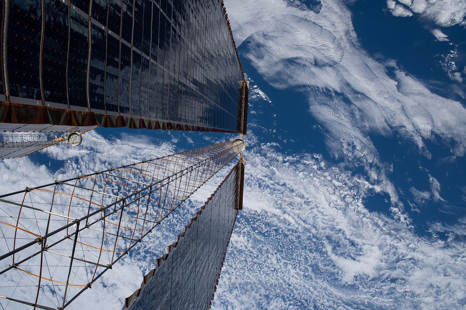Looking down a pair of the International Space Station's roll-out solar arrays with Earth's clouds below